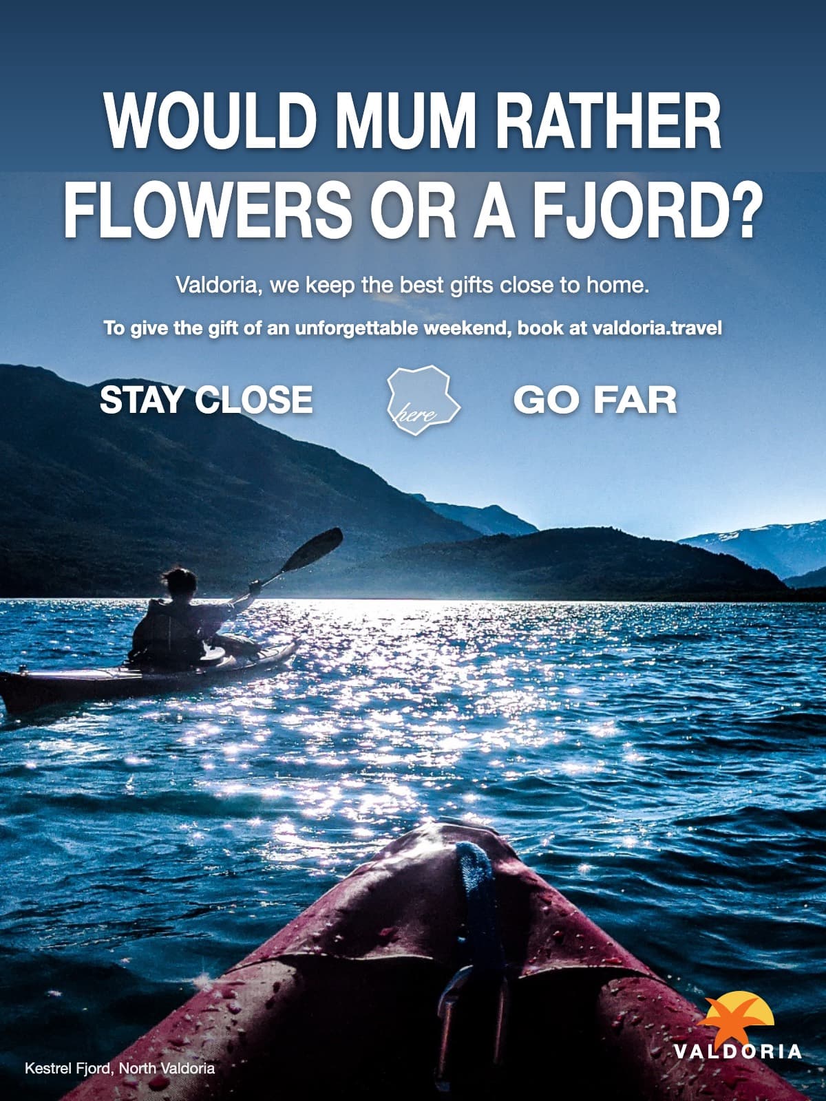 An advertisement for Valdoria's national tourism board: a photograph taken over the bow of the viewer's own kayak, following a lone paddler across a calm lake towards snow-capped mountains, sun scattered on the water; the headline ‘Would Mum rather flowers or a fjord?’ sits in the sky.