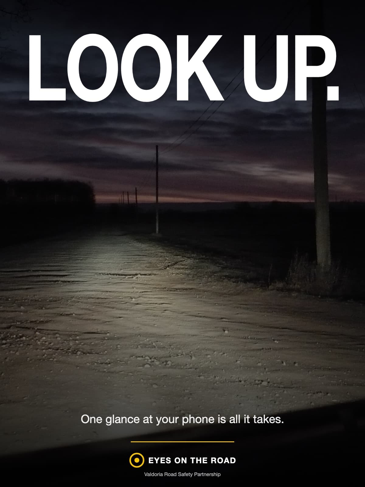 A road-safety poster: a driver's-eye view of an empty country road at night, lit only by headlights; across the dark sky, in huge white capitals, ‘LOOK UP.’; small text near the foot: ‘One glance at your phone is all it takes.’ and a yellow ‘Eyes on the road’ logo.