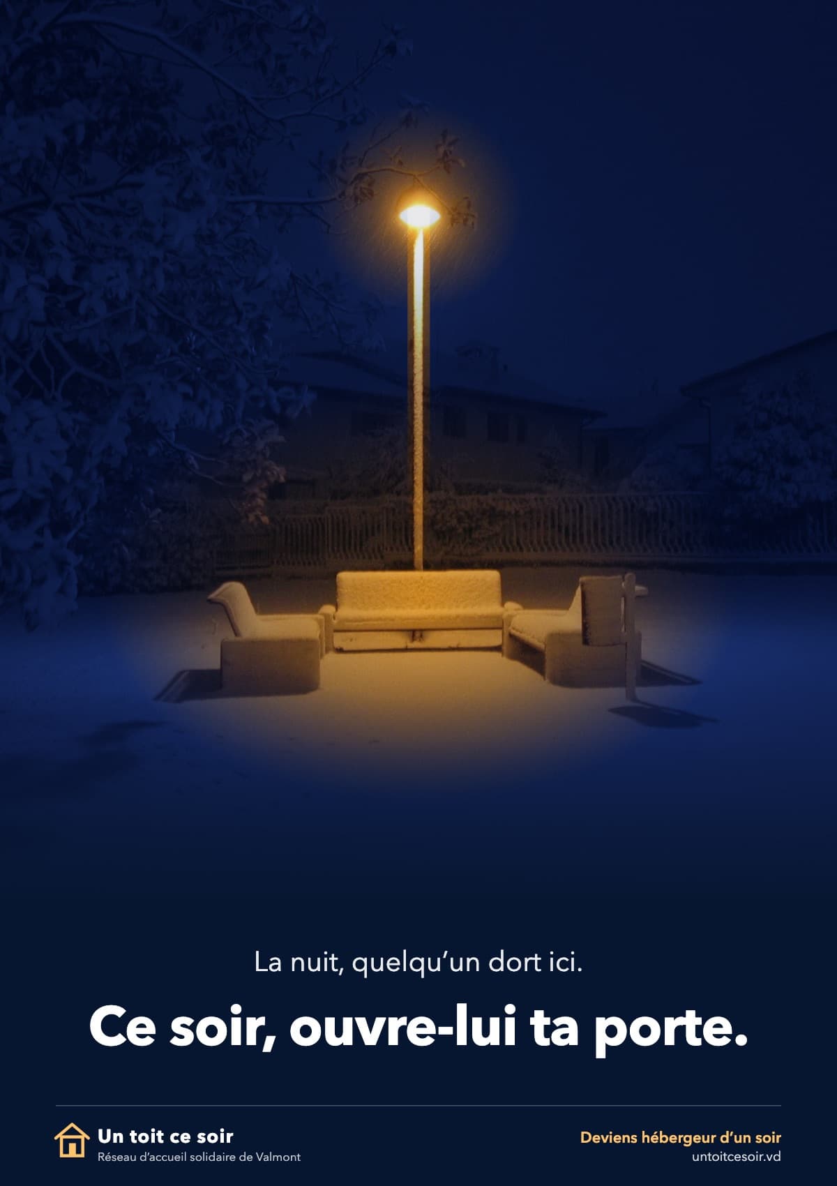 Affiche verticale sur fond bleu nuit. Photographie : la nuit, dans un petit square enneigé, un seul réverbère allumé éclaire des bancs vides couverts de neige ; toute l’image est d’un bleu sombre, sauf la lumière chaude, orangée, sous la lampe. En bas, en petites lettres blanches : « La nuit, quelqu’un dort ici. », puis, en grandes lettres blanches : « Ce soir, ouvre-lui ta porte. » Tout en bas, le logo d’une maison et « Un toit ce soir · Réseau d’accueil solidaire de Valmont » ; à droite, « Deviens hébergeur d’un soir · untoitcesoir.vd ».