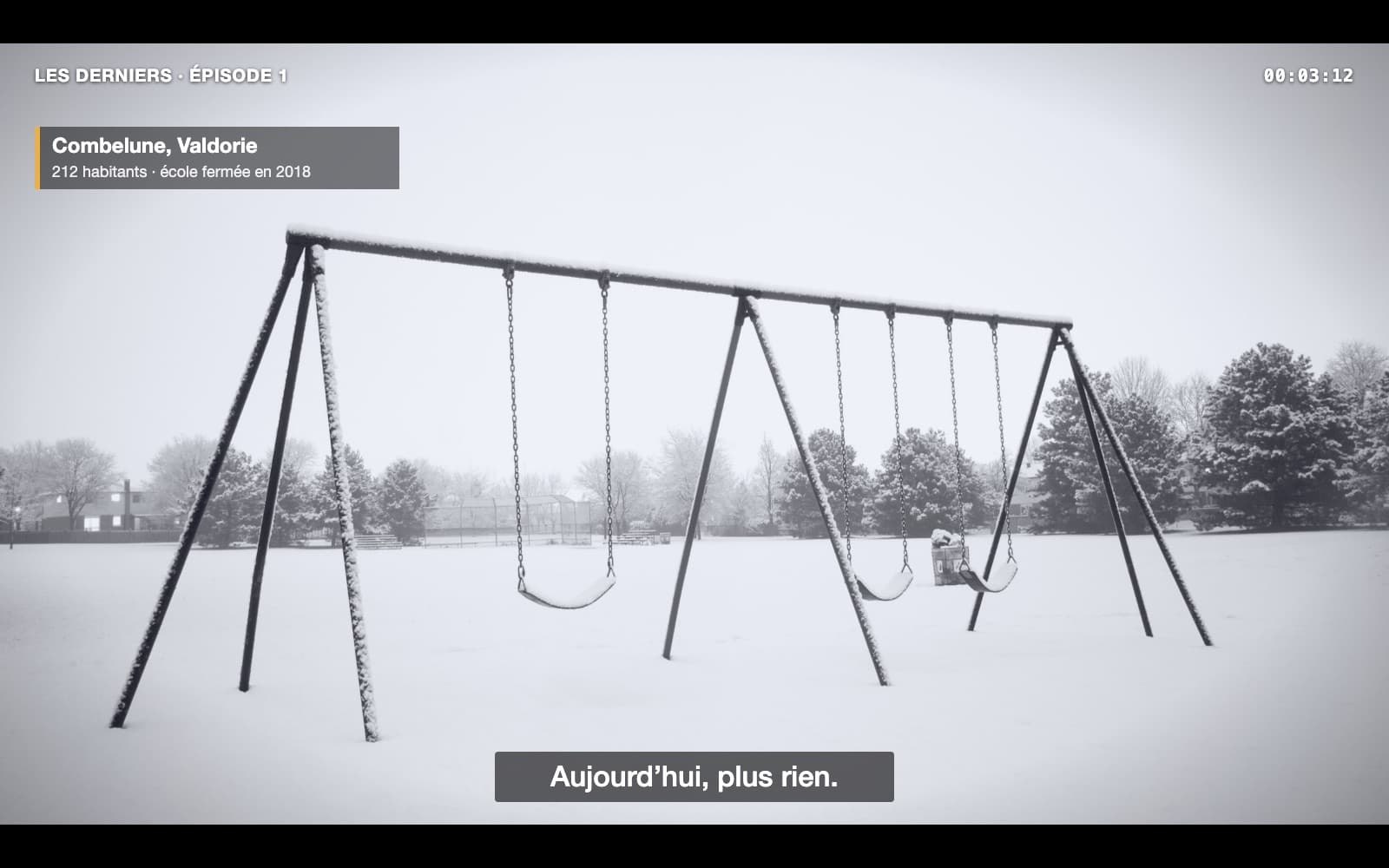 Une image 16:9 tirée d’un documentaire : un portique de balançoires en métal, vide, au milieu d’un grand terrain couvert de neige, cadré en plan large. La neige s’est posée sur la barre et sur les trois sièges ; aucune trace de pas. Au fond, des arbres enneigés sous un ciel blanc ; au loin à gauche, à peine visible, une maison aux fenêtres allumées. En haut à gauche : « LES DERNIERS · ÉPISODE 1 » ; en haut à droite, le minutage 00:03:12 ; en dessous, un cartouche « Combelune, Valdorie — 212 habitants · école fermée en 2018 ». Sous-titre : « Aujourd’hui, plus rien. » Transcription : VOIX OFF (sur ce plan) : Ici, autrefois, on entendait les enfants. (silence) Aujourd’hui, plus rien. — Plan suivant, TÉMOIN (une habitante, face caméra) : Ils sont tous partis. Moi, je reste. Pour qui ?