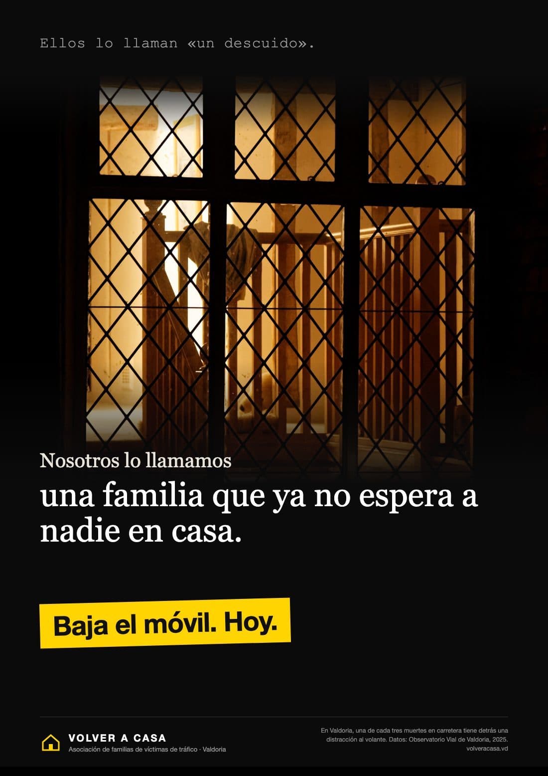 Octavilla vertical de fondo negro. Arriba, en letra de máquina de escribir, gris y pequeña: «Ellos lo llaman «un descuido».». En el centro, la foto de una ventana de cuarterones encendida de noche: a través del cristal se ve una luz cálida, una escalera de madera y un recibidor vacío, sin nadie. Debajo, en blanco: «Nosotros lo llamamos» y, en letras grandes, «una familia que ya no espera a nadie en casa.». Más abajo, una franja amarilla ligeramente inclinada, como una cinta pegada, con «Baja el móvil. Hoy.» en negro. Al pie, el logo de una casita amarilla «VOLVER A CASA · Asociación de familias de víctimas de tráfico · Valdoria» y, en letra diminuta, un dato con su fuente.